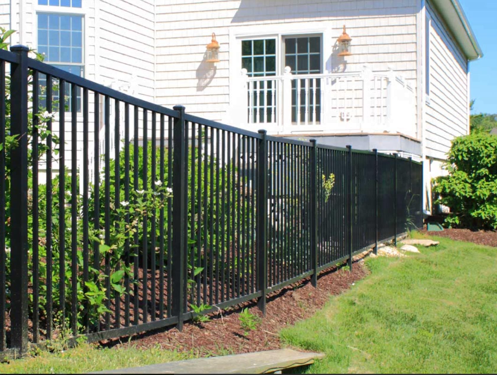 A sleek black metal fence elegantly borders the white house, complementing its charming porch and lush green lawn.