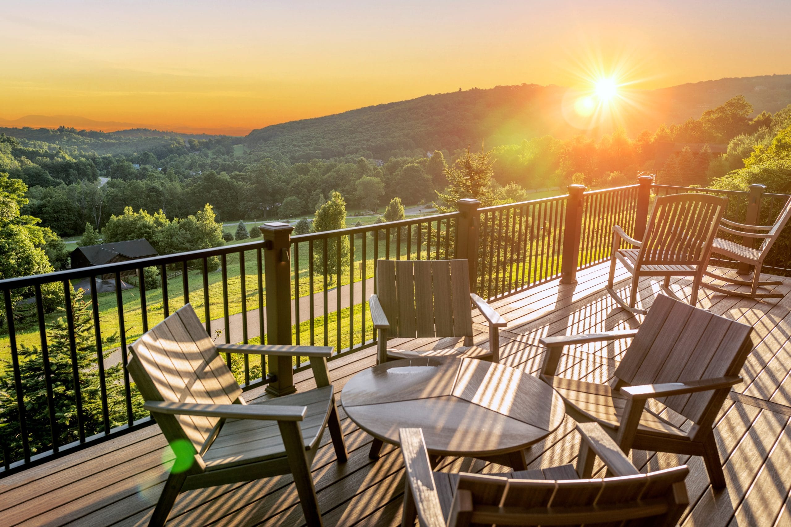 Beautiful dawn sunshine breaking over hills with wooden balcony Wooden deck with chairs overlooking a lush green valley and hills at sunset. Sunlight casts long shadows.